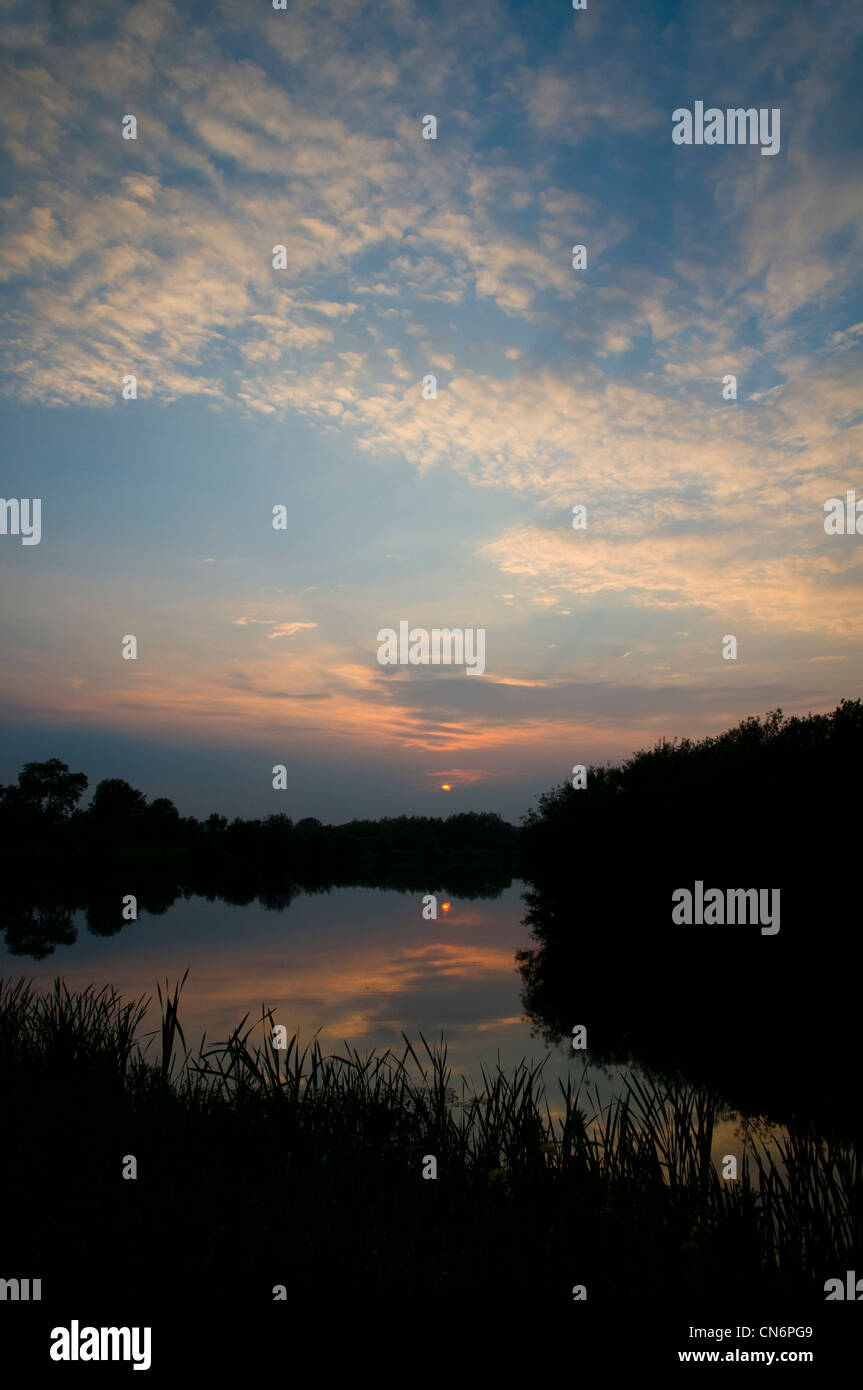The sun setting below cirrocumulus clouds at Priory Water Nature Reserve, Leicestershire. Stock Photo