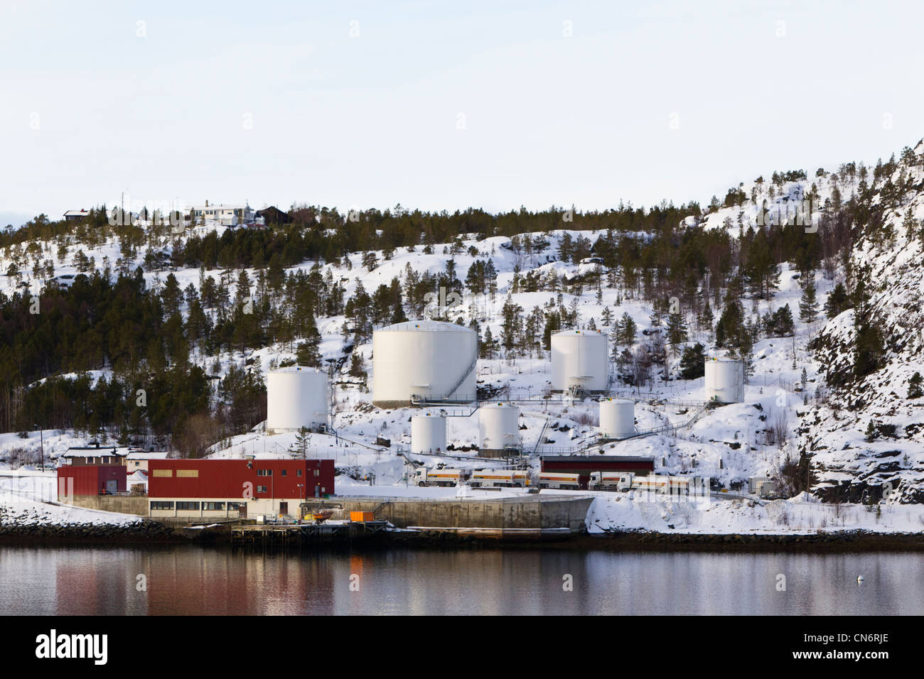 An oil storage facility on the shores of a fjord with a snow covered mountain behind taken in landscape format Stock Photo