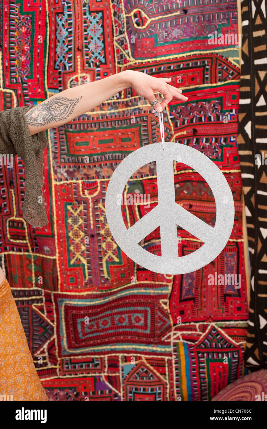 A woman's hand holding a peace sign in front of a South American and African tapestry as a symbol of world peace. Stock Photo