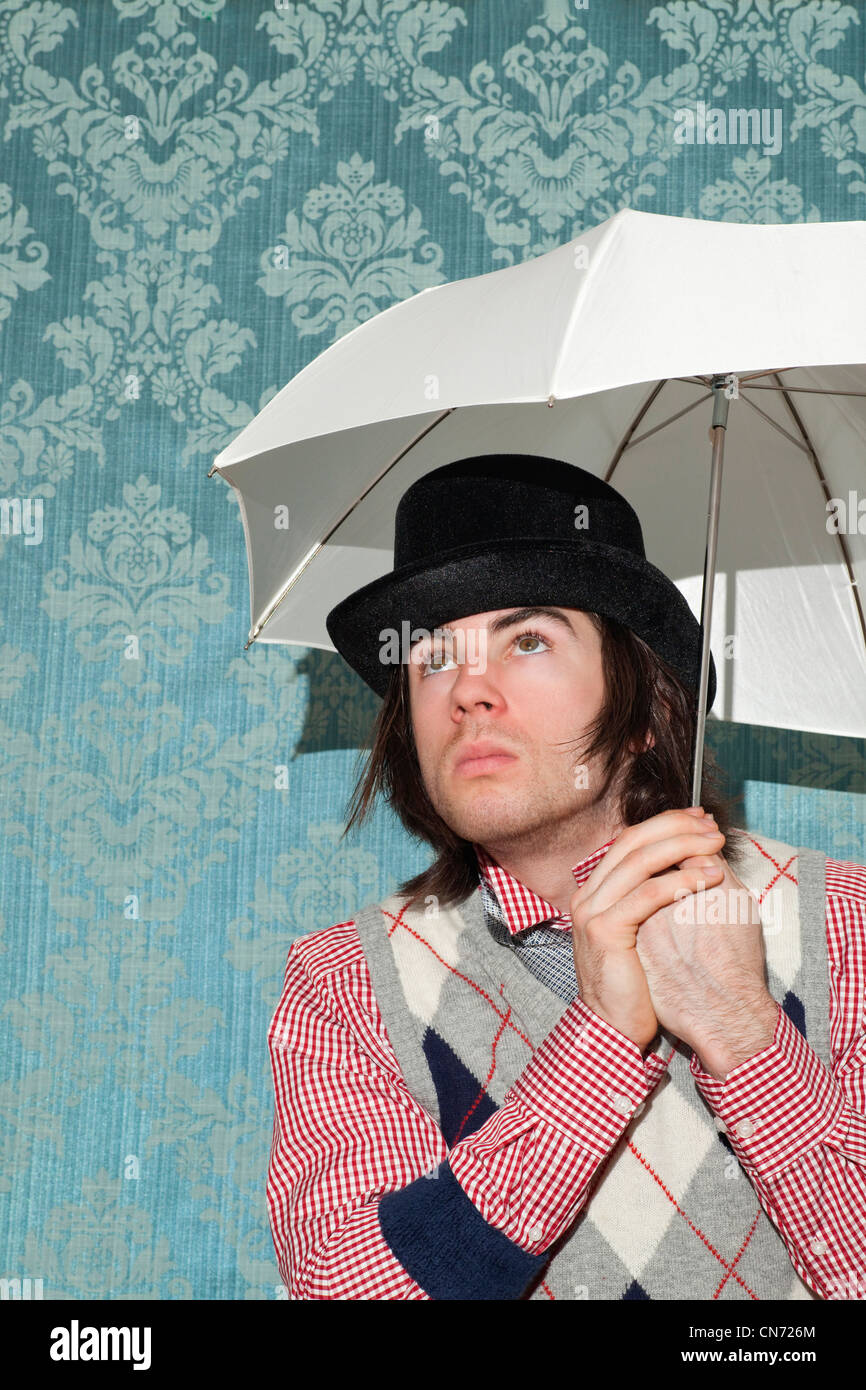 Portrait of young caucasian man holding white umbrella and wearing hat indoors with wallpaper