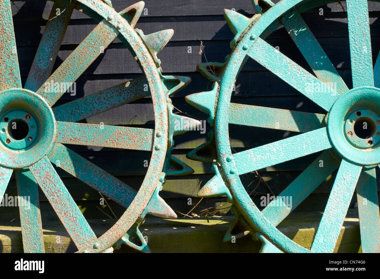 Large iron tractor wheels leaning against a barn. These may be from a