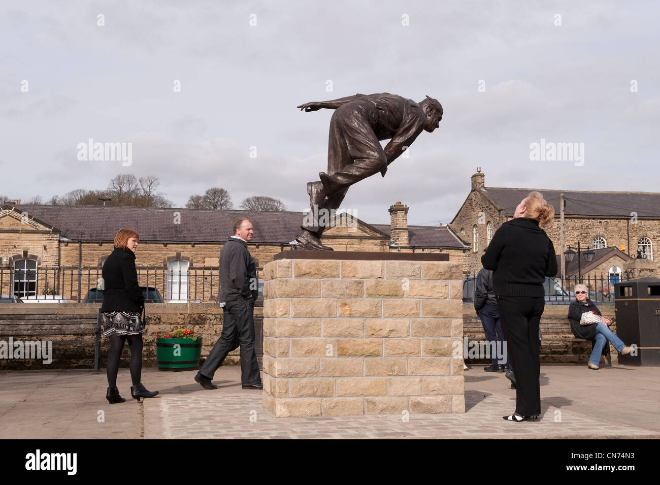 People standing, looking, walking by bronze statue of cricketer Fred (Freddie) Trueman (fast bower bowling) - Skipton, North Yorkshire, England UK Stock Photo