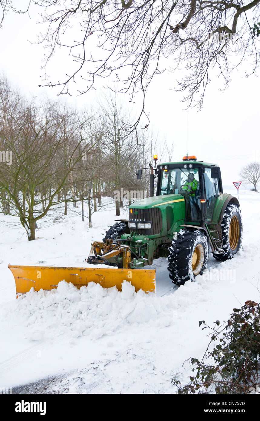 A tractor, mounted with a snow plough, clearing snow from a country