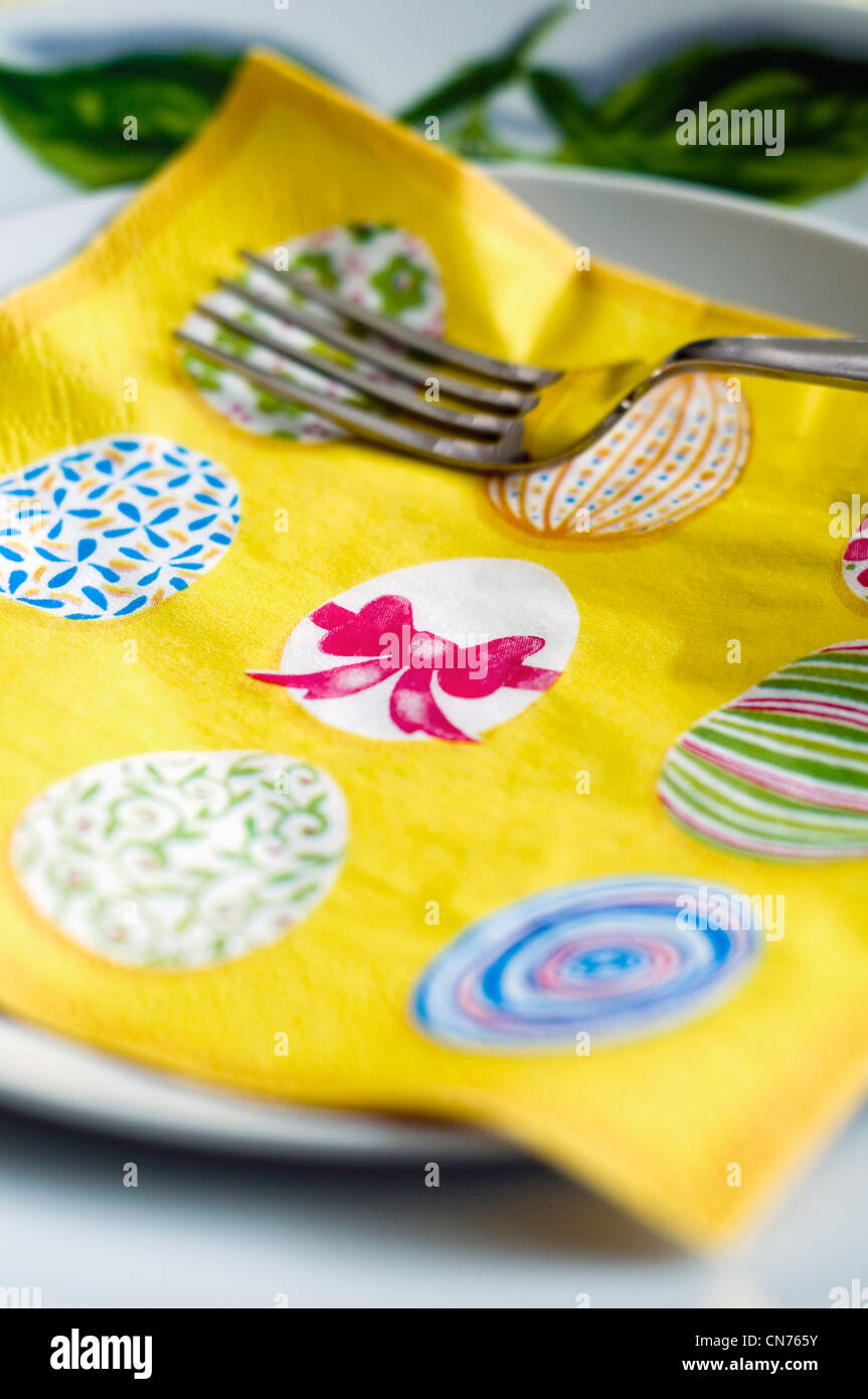 A yellow serviette decorated with an Easter design resting on a dinner plate Stock Photo