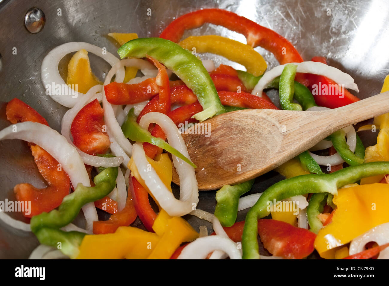 Closeup of sliced peppers and onions being stir fried in a stainless steel wok pan. Stock Photo