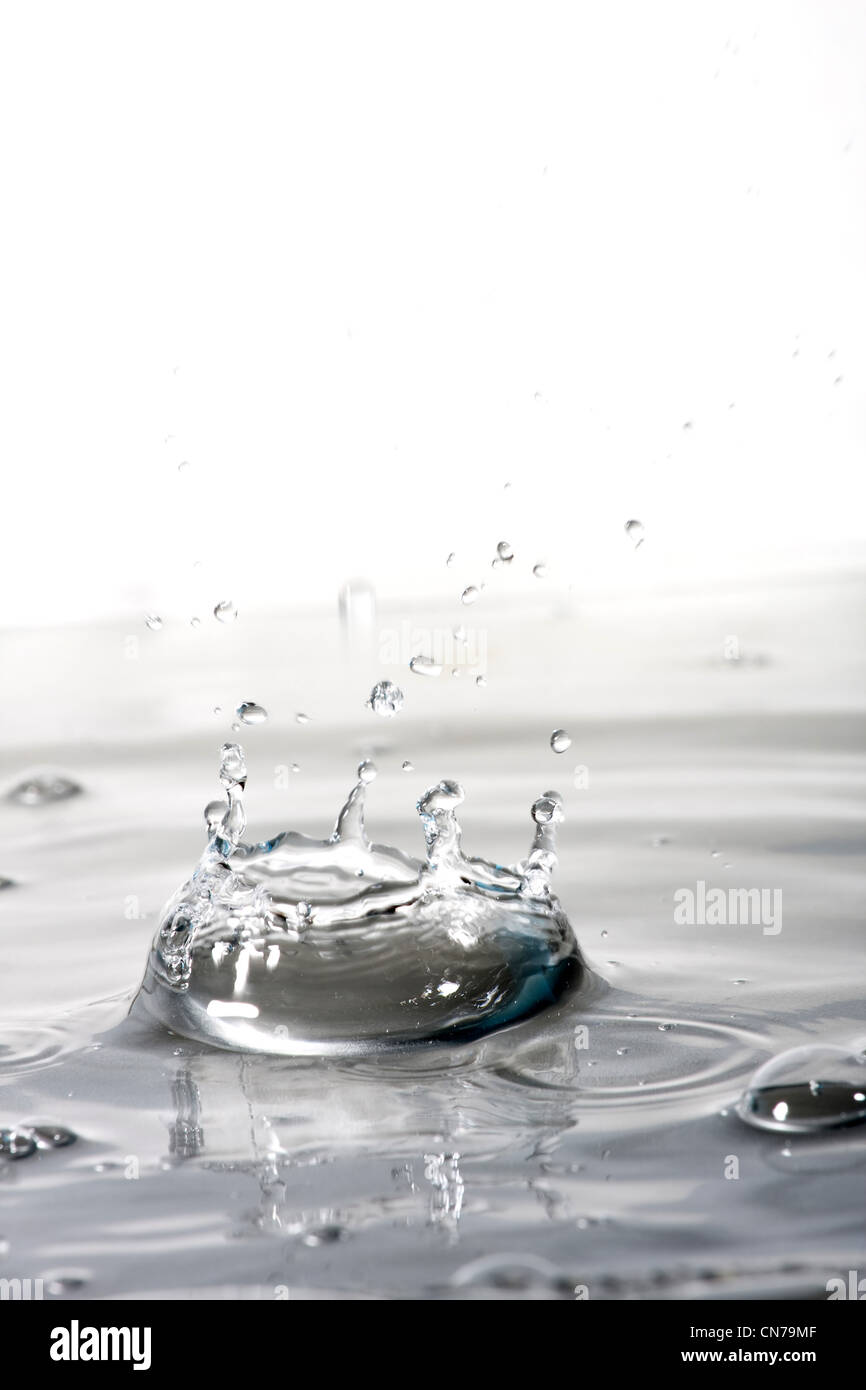 A clear water background texture and splash with droplets forming a crown shape. Shallow depth of field. Stock Photo