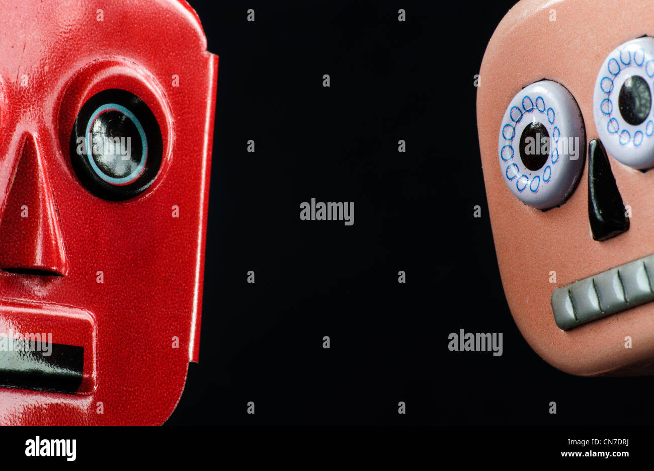 Close up of the faces of two metal, wind-up robots on a black background. Stock Photo