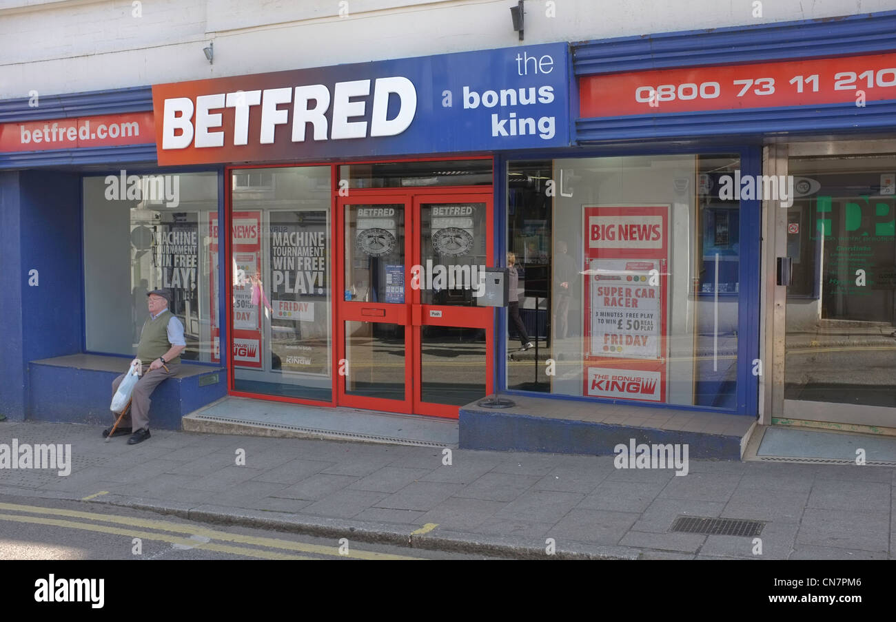 A man sits outside a betting shop in Helston, Cornwall Stock Photo