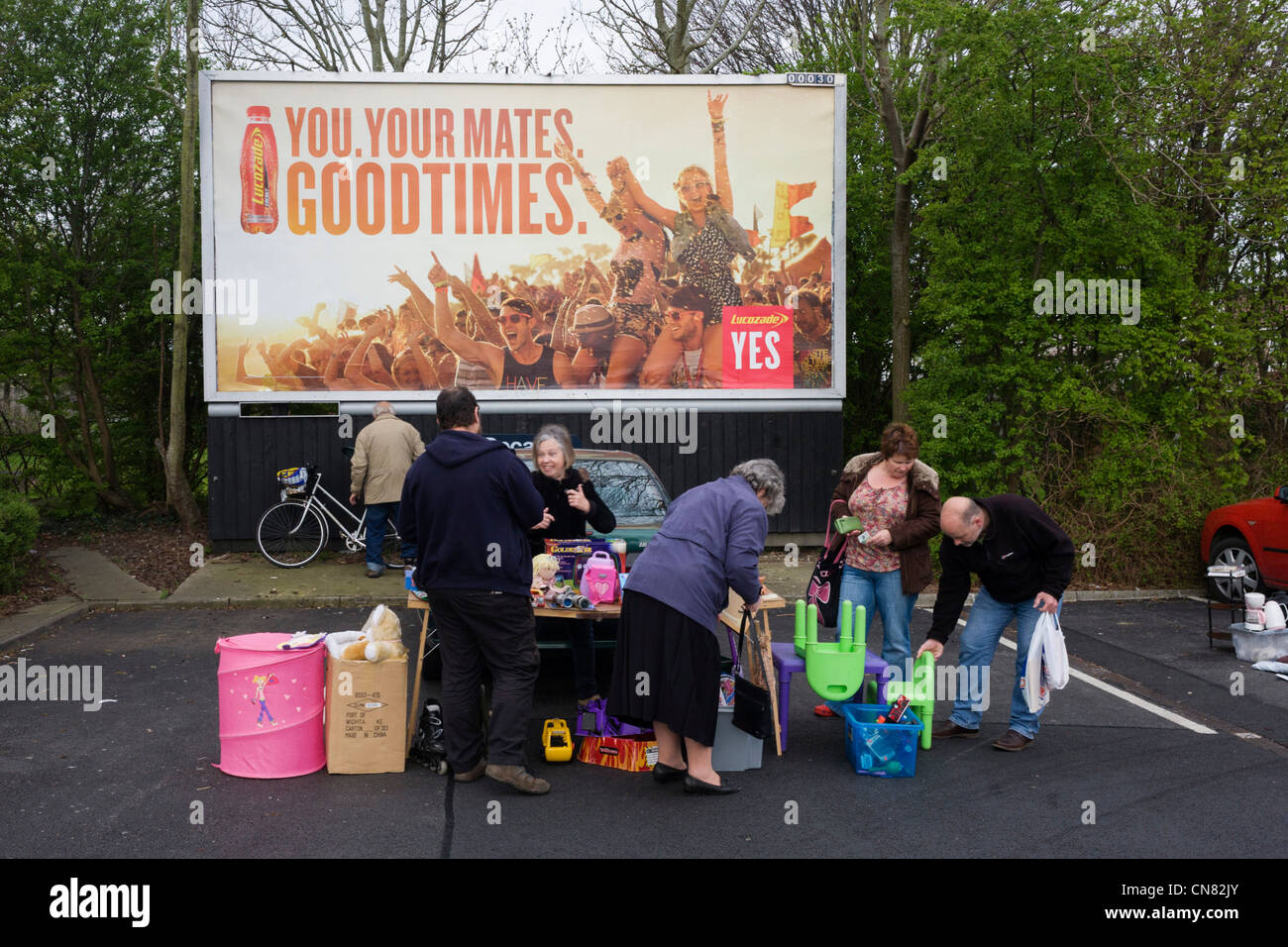 Locals sift through possessions below a Goodtimes ad during a Sunday car boot sale in a supermarket car park. Stock Photo