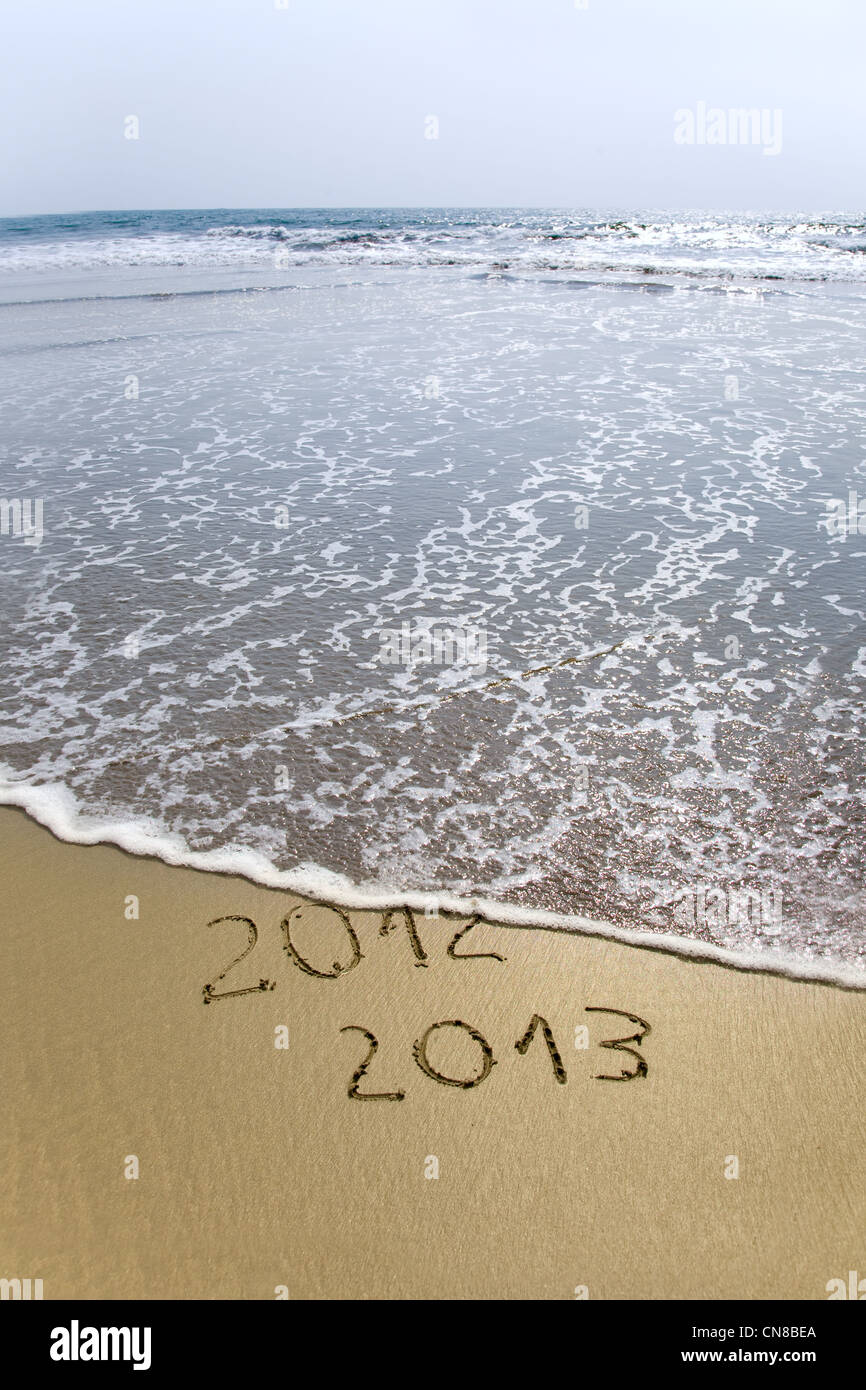 2012 and 2013 written in sand on beach with sea waves starting to erase the word Stock Photo