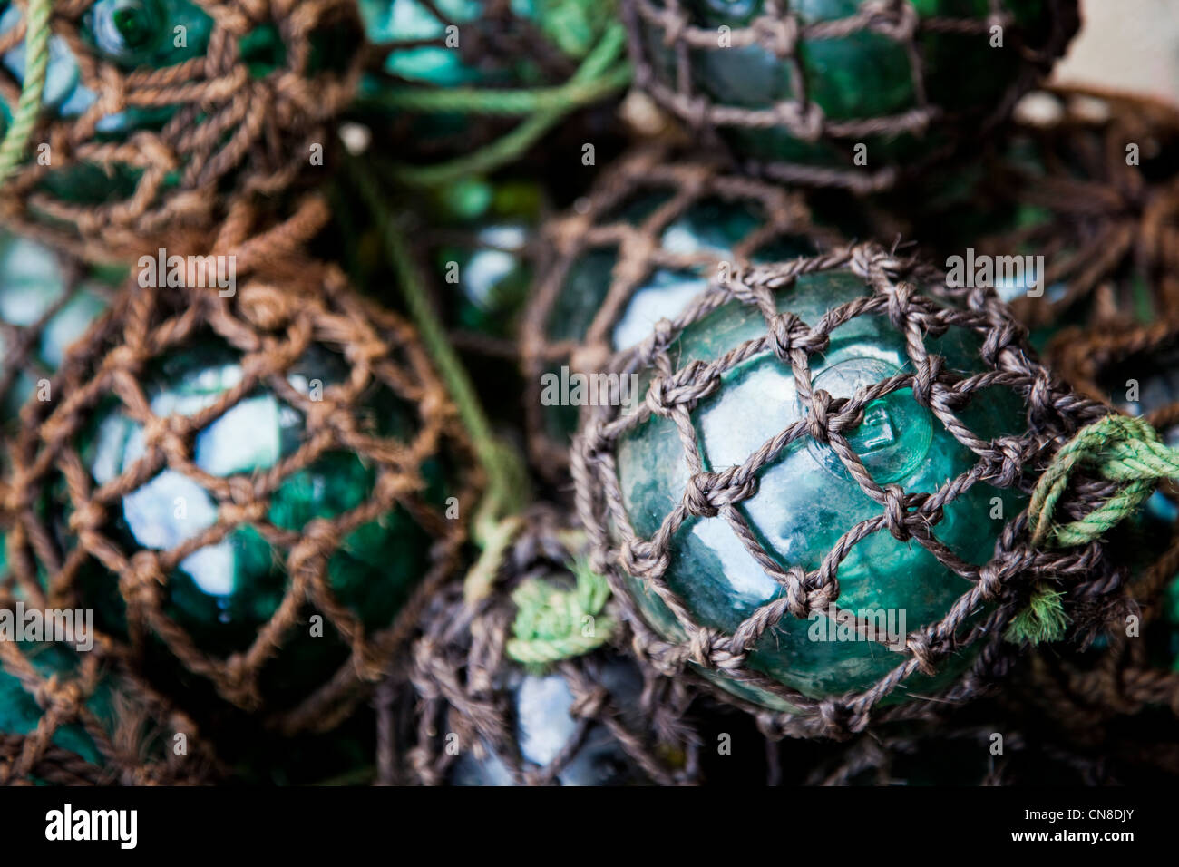 Closeup of old fishing nets, green rounded stone sinkers and glass floats  in a glimpse of sunlight. - stock…