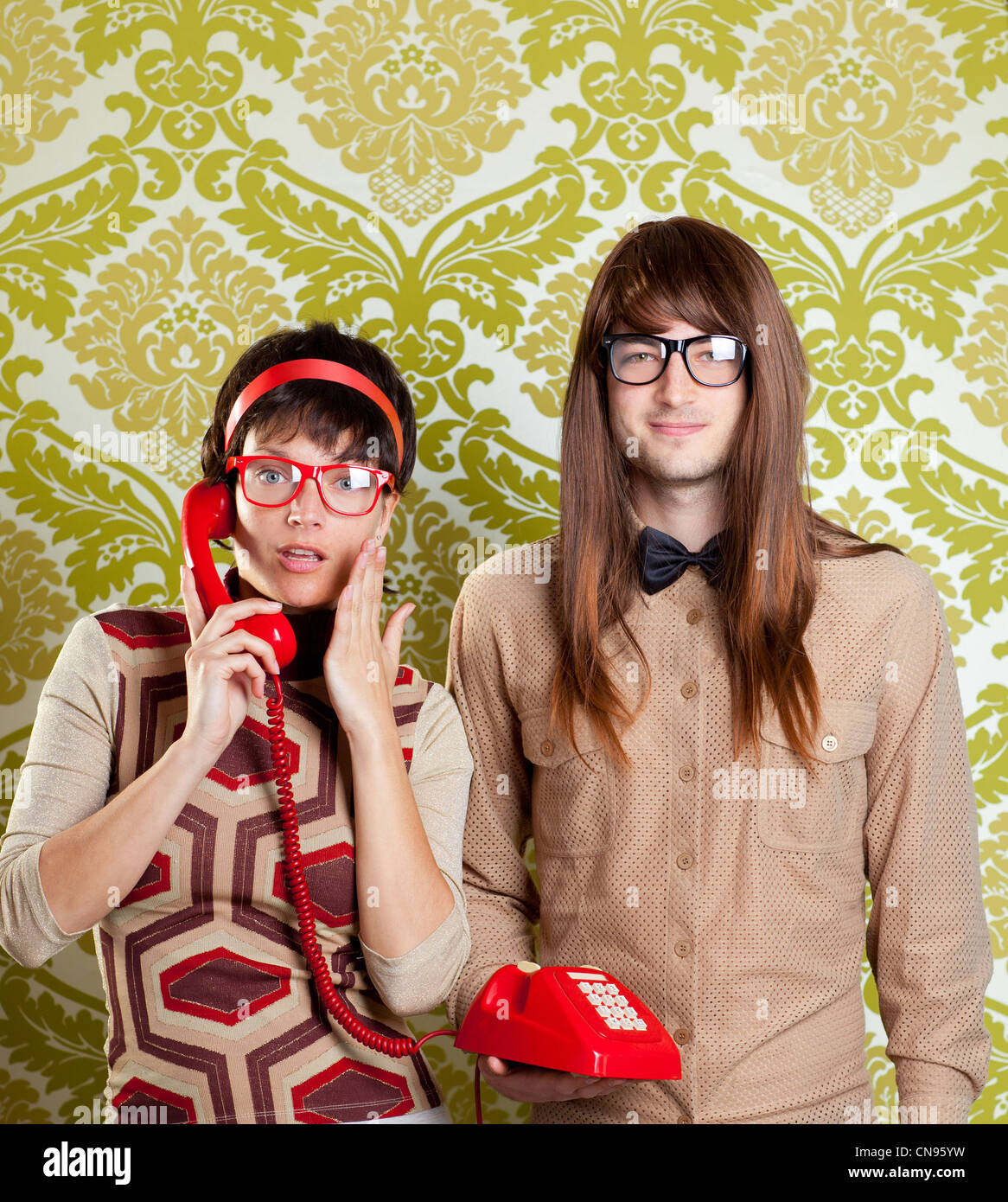 funny nerd humor couple talking retro vintage red telephone on wallpaper Stock Photo