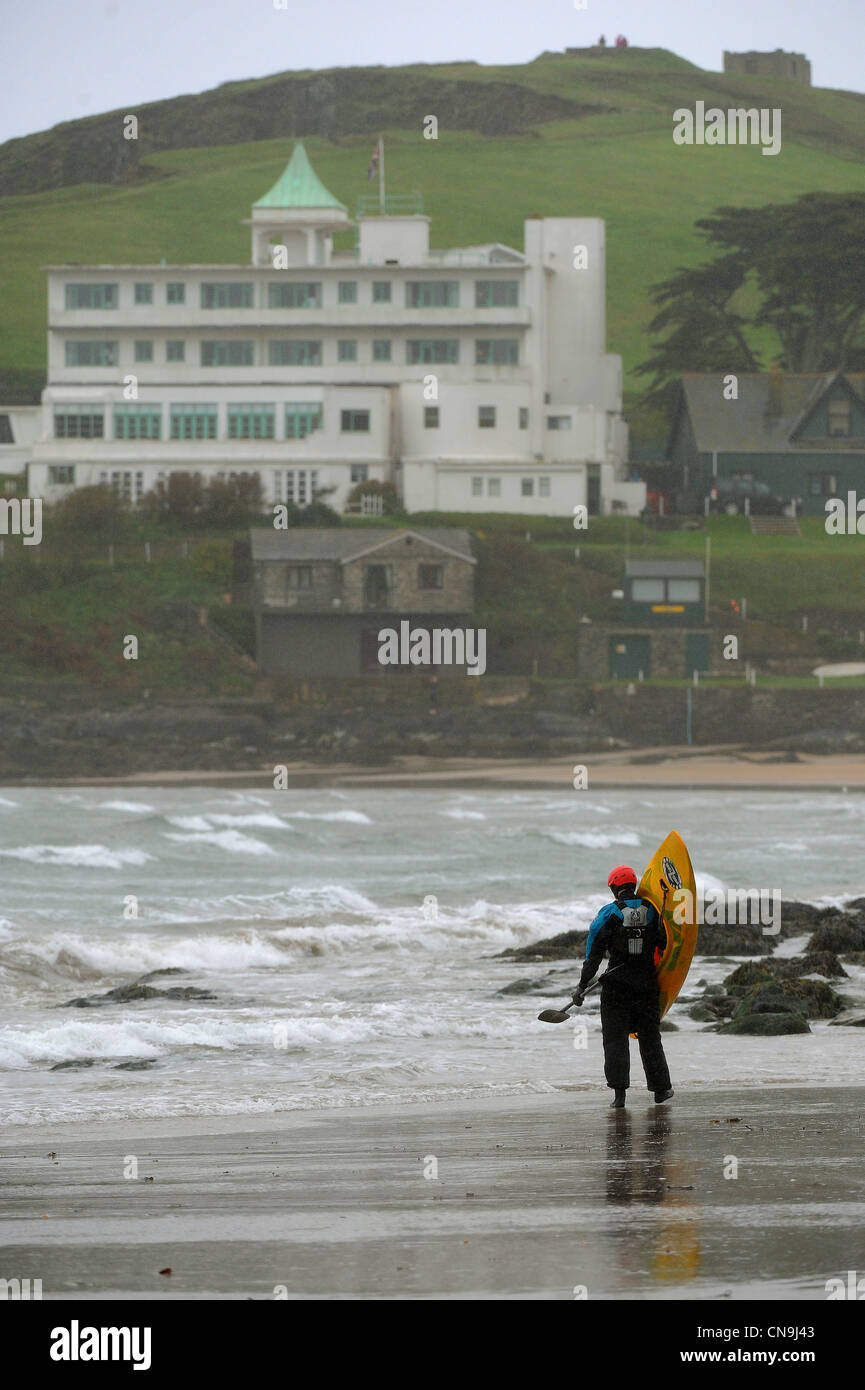 A lone kayaker walks down the beach at Bigbury-on-Sea in South Devon towards the Burgh Island Hotel as gale force winds and rain Stock Photo