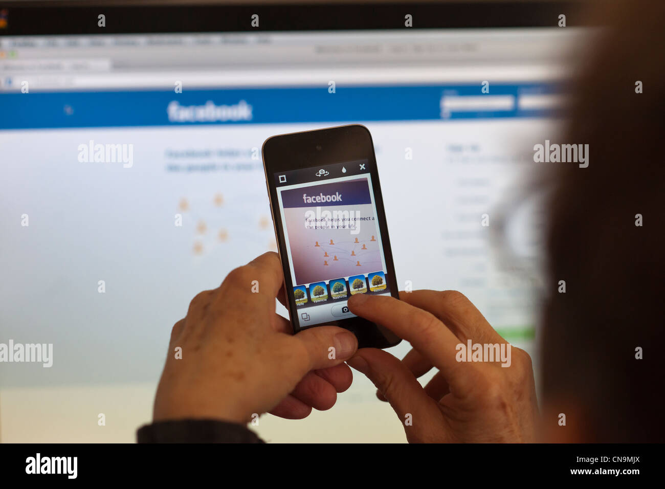 A woman holds her iPod touch and photographs the Facebook web page using an Instagram app Stock Photo