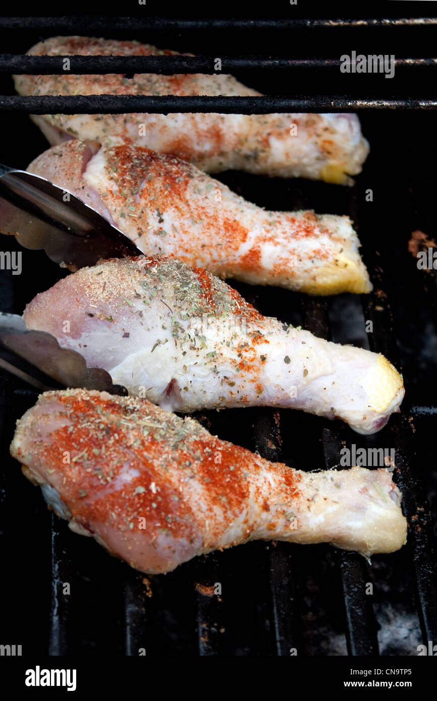 Raw chicken drumstick legs being places on the gas grill to cook. Shallow depth of field Stock