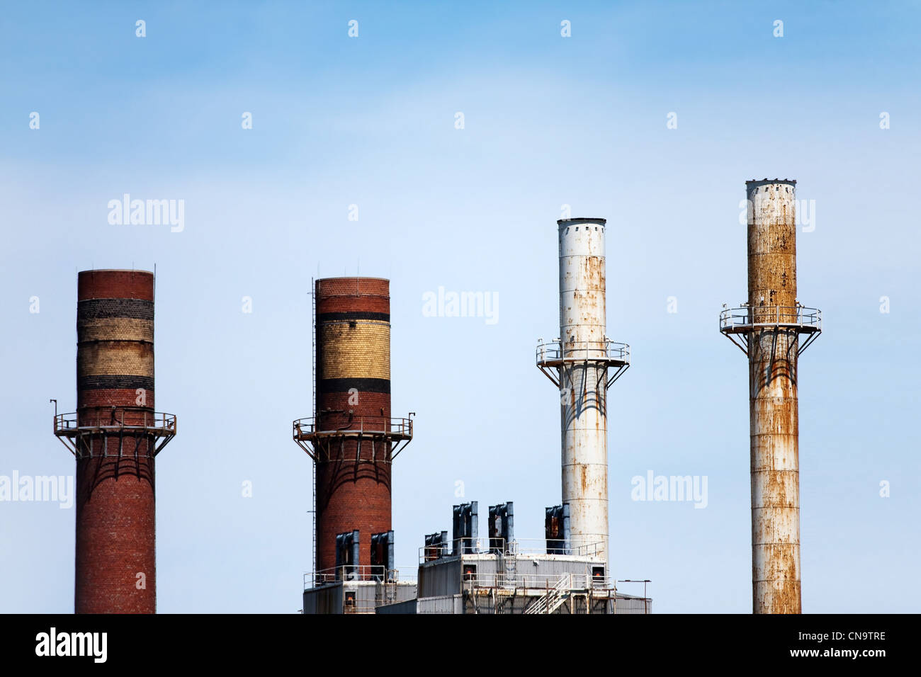 Four smoke stacks atop factories or industrial buildings in the skyline. Stock Photo
