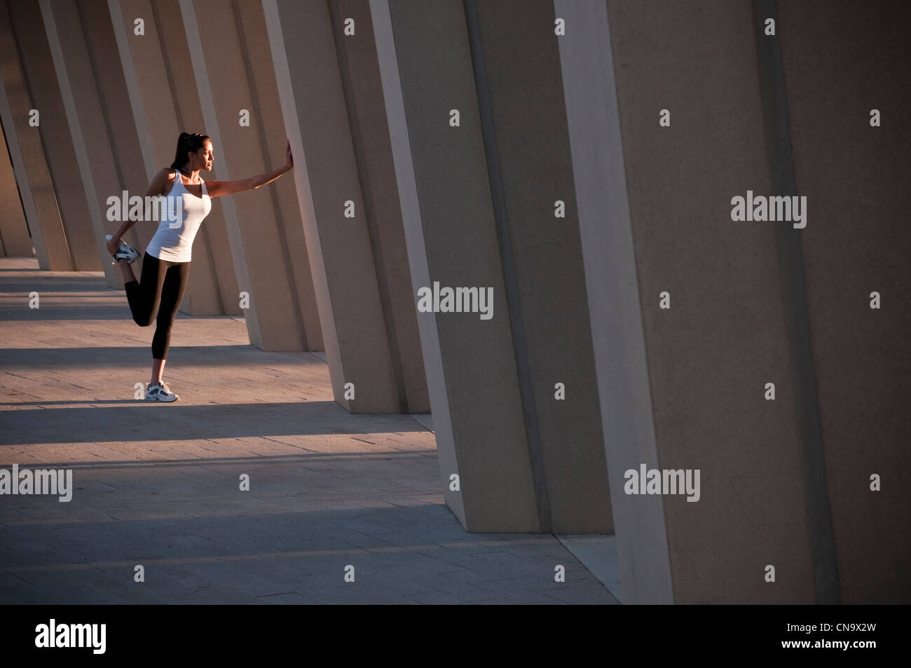 Runner stretching on concrete pillar Stock Photo