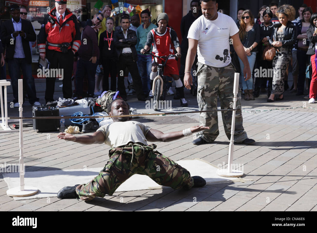 Street entertainers limbo dancing under a low pole with an audience of people watching in Leeds city centre Yorkshire England UK Stock Photo