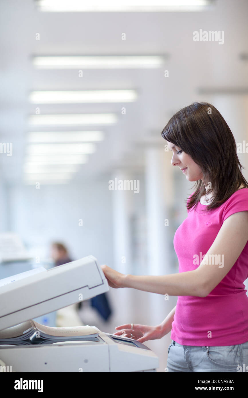 pretty young woman using a copy machine (shallow DOF; color toned image) Stock Photo