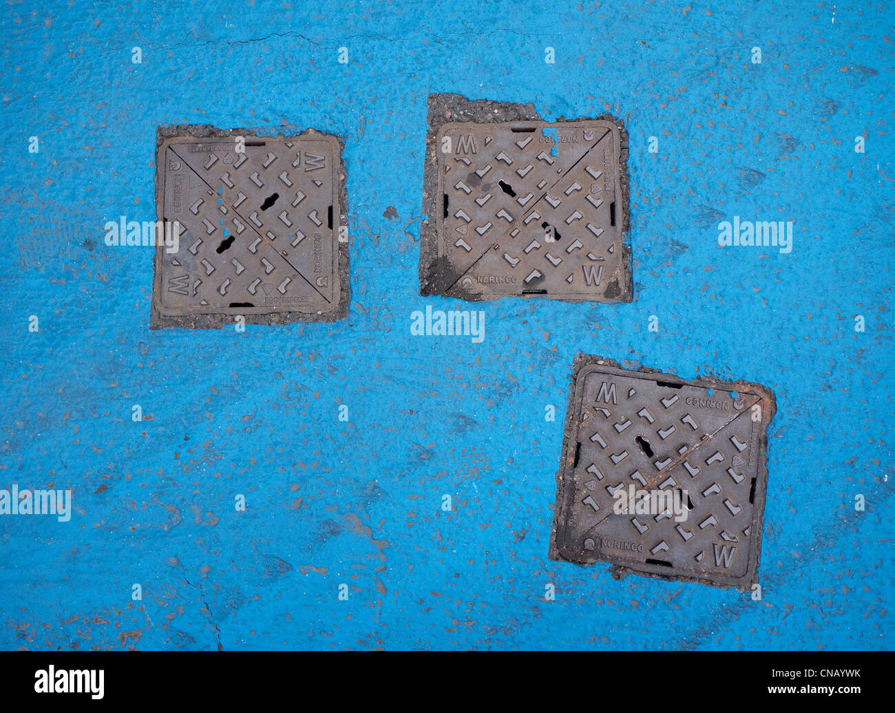 three metal drain covers on blue painted tarmac Stock Photo