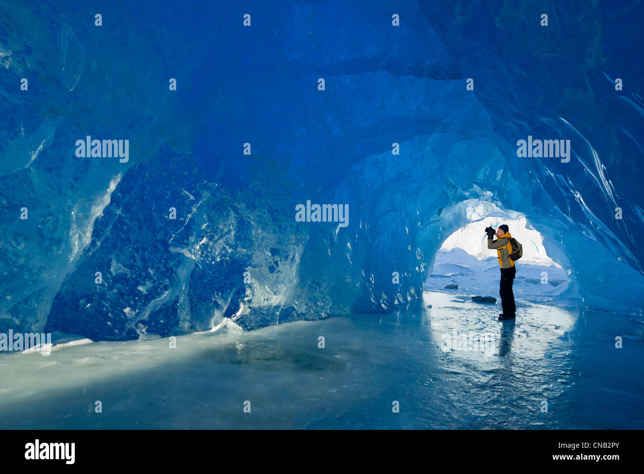 Man photographs inside an ice cave of an iceberg frozen in Mendenhall Lake, Juneau, Southeast Alaska, Winter Stock Photo