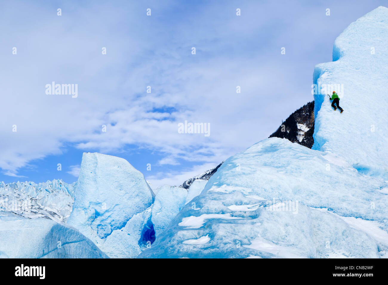 Ice climber with ice axe climbs the face of a large iceberg frozen in Mendenhall Lake, near Juneau, Southeast Alaska, Winter Stock Photo