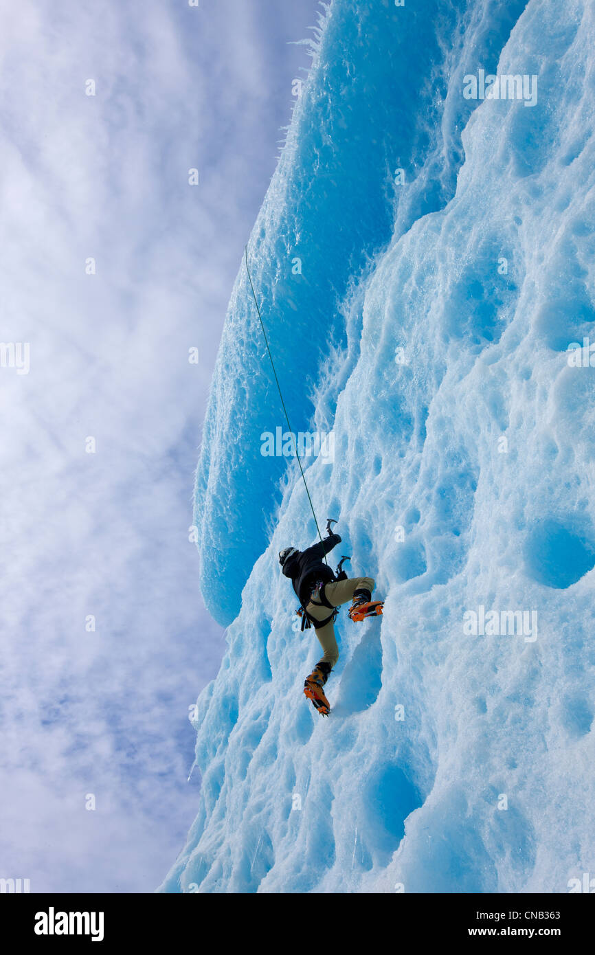 An ice climber ascends the face of a large iceberg frozen into Mendenhall Lake, Juneau, Southeast Alaska, Winter Stock Photo