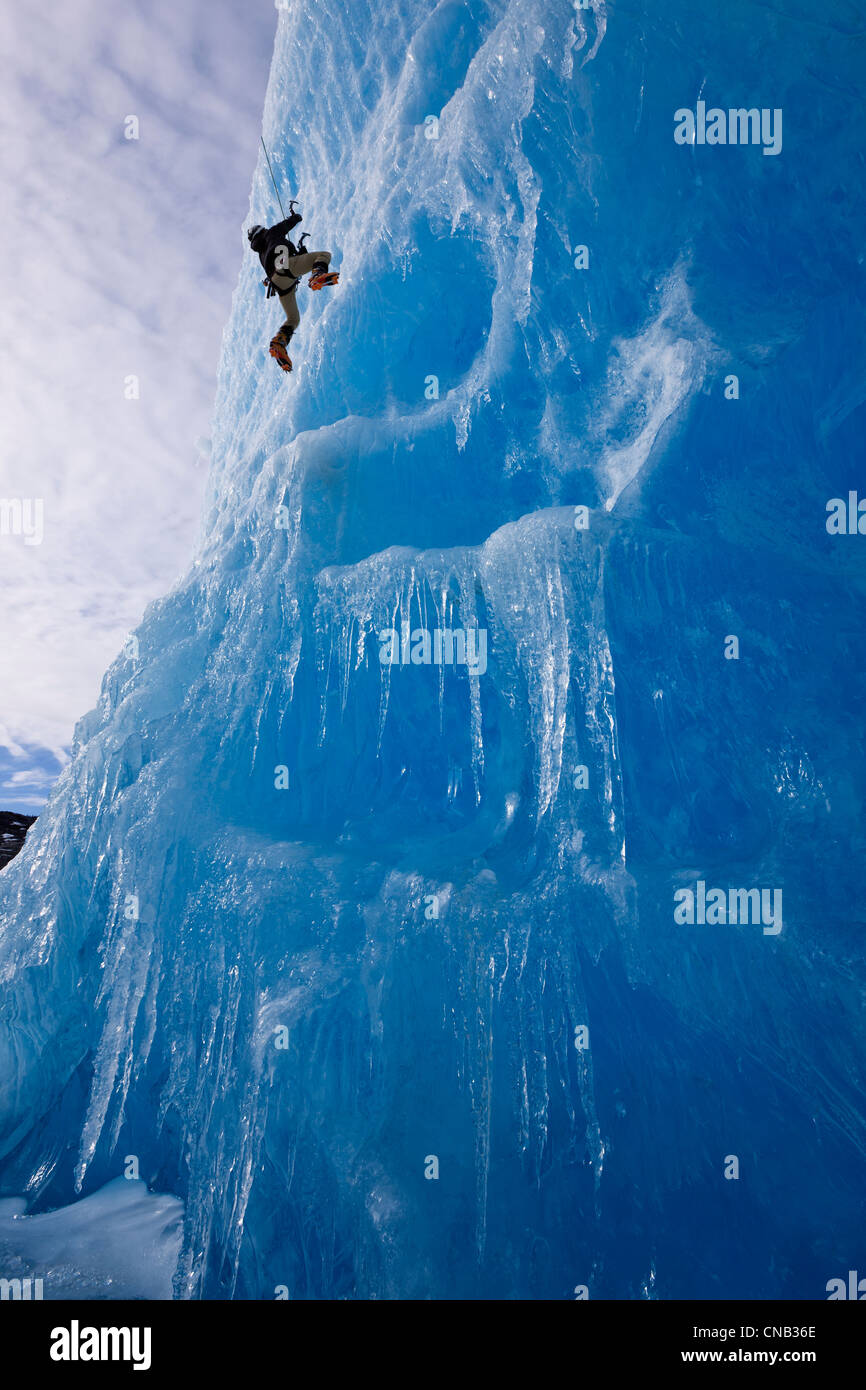 An ice climber ascends the face of a large iceberg frozen into Mendenhall Lake, Juneau, Southeast Alaska, Winter Stock Photo