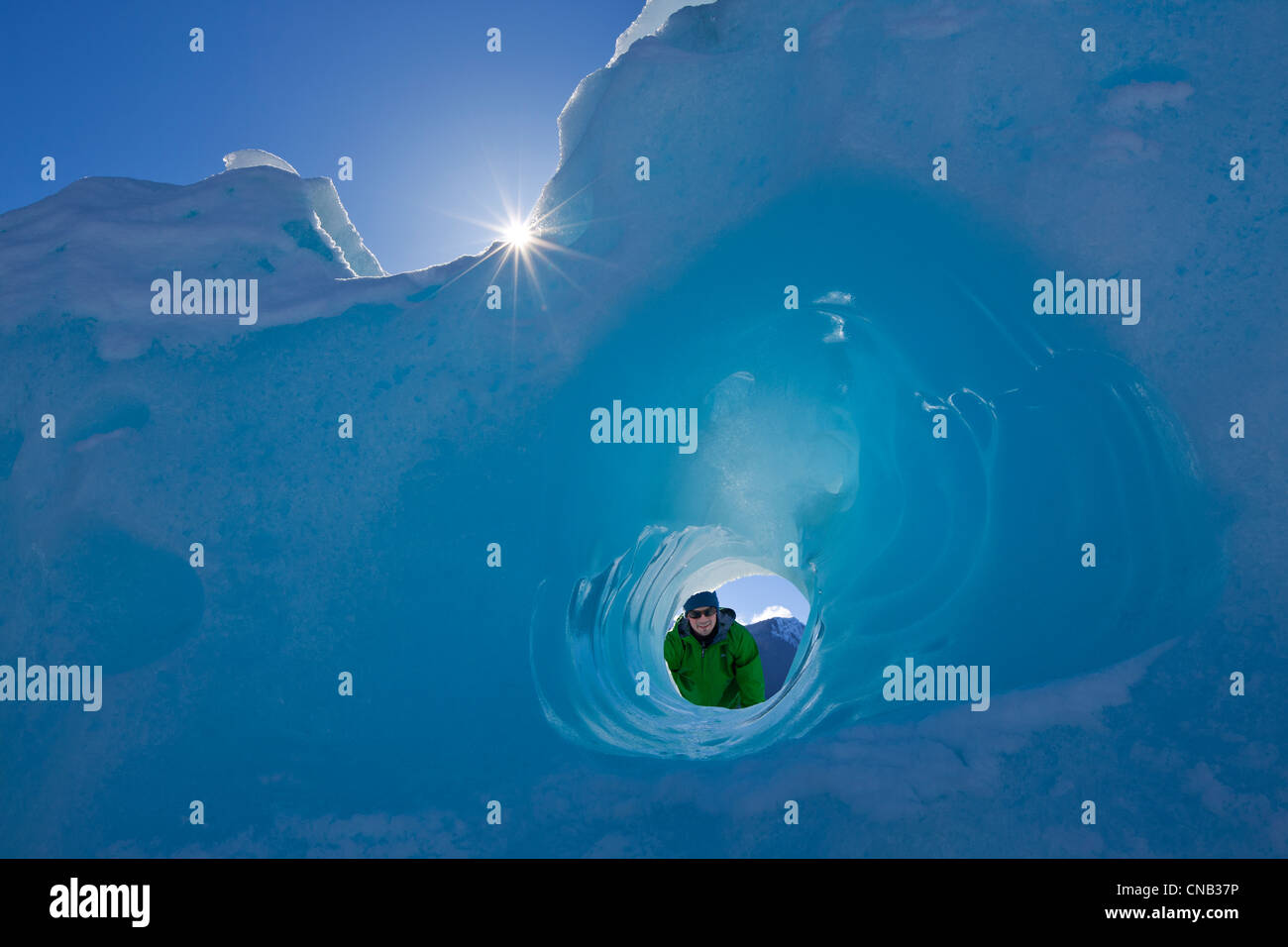 COMPOSITE: Person looking through a small tunnel eroded in an iceberg frozen in Mendenhall Lake, Juneau, Alaska, Winter Stock Photo