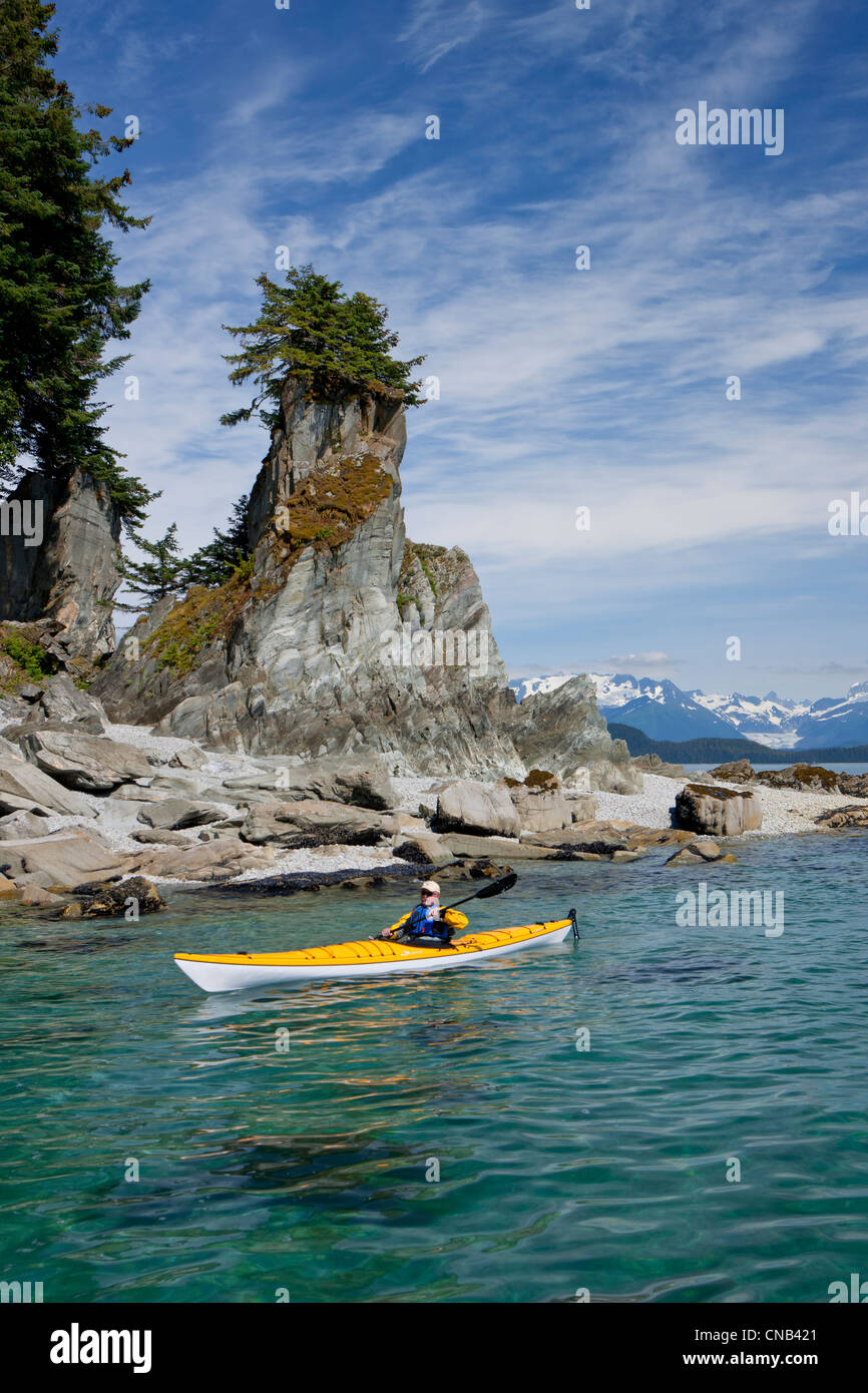 A water level view of a sea kayaker paddling in calm waters along a shoreline near Juneau, Inside Passage, Alaska Stock Photo