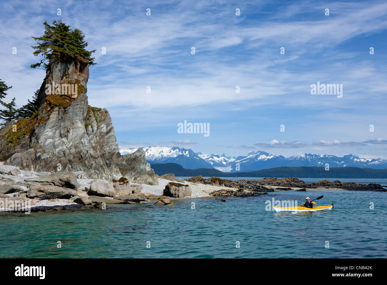 A water level view of a sea kayaker paddling in calm waters along a shoreline near Juneau, Inside Passage, Alaska Stock Photo
