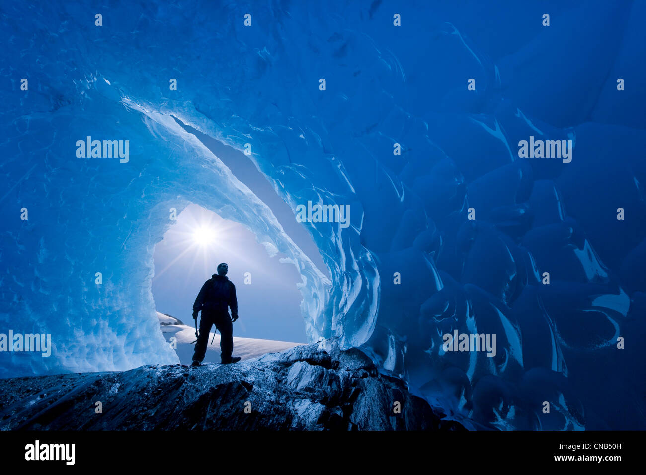 COMPOSITE: View from inside an ice cave of an iceberg frozen in Mendenhall Lake as an ice climber stands at the entrance, Alaska Stock Photo