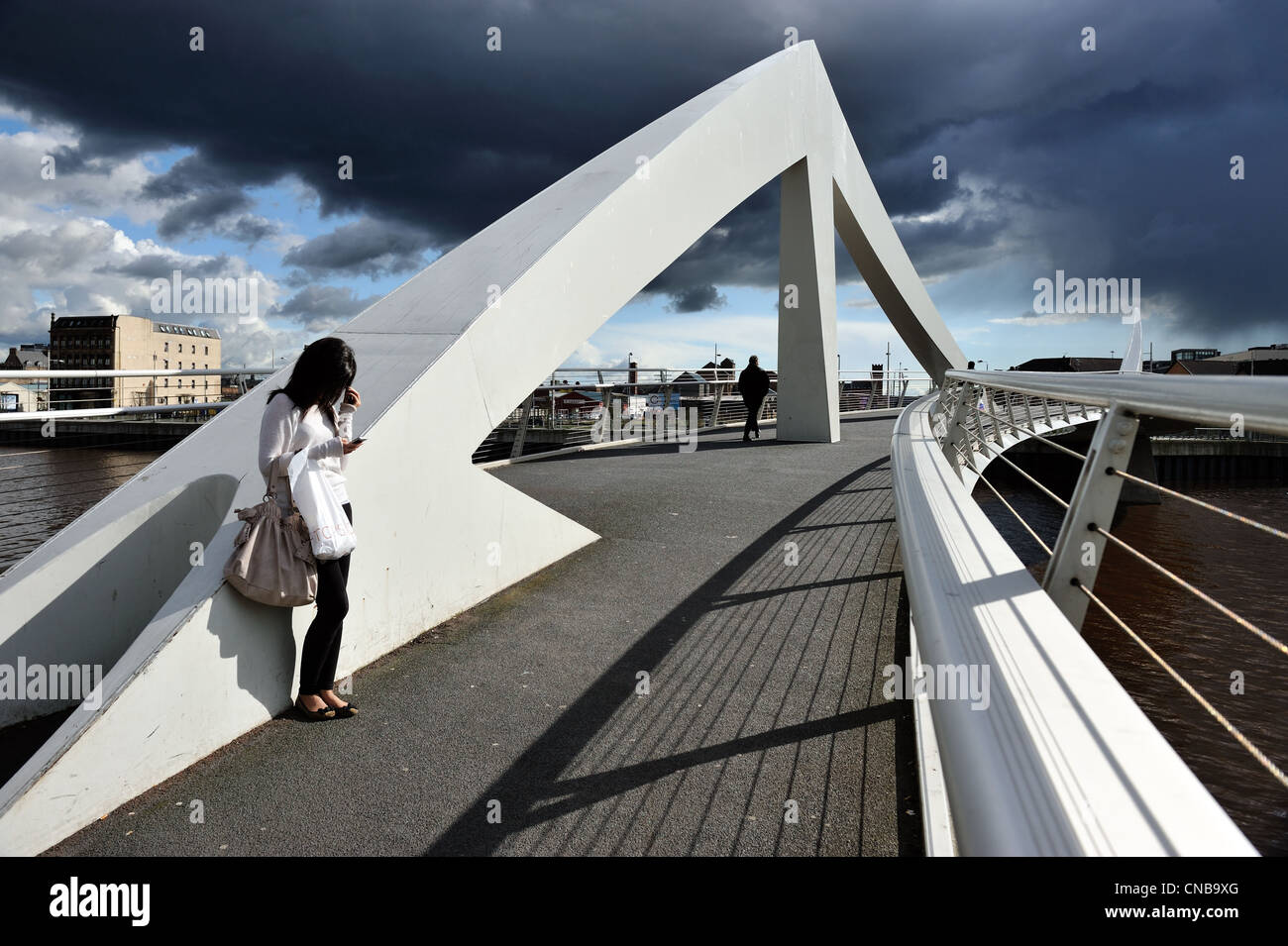 A girl stands in the sun on the Squiggly Bridge (Broomielaw-Tradeston Bridge) as dark clouds gather in the Glasgow sky. Stock Photo