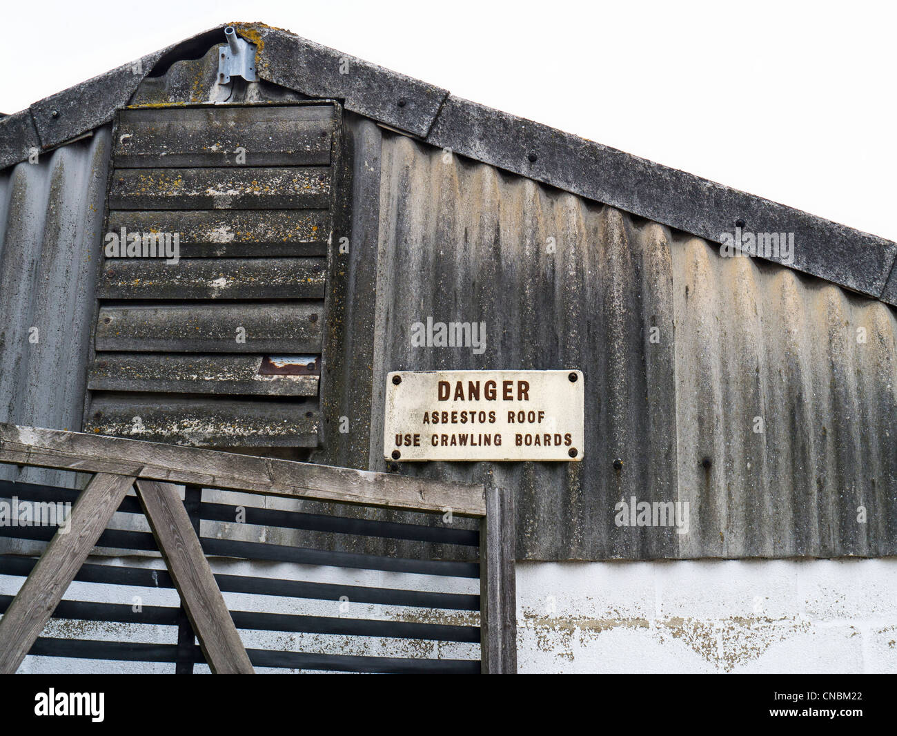 Danger Sign on an Industrial Building with Corrugated Asbestos Roof and Wall Stock Photo