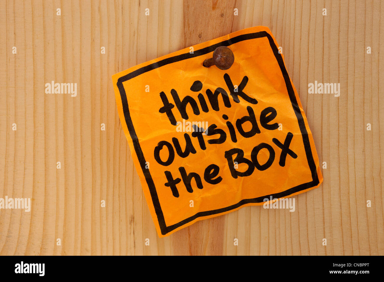think outside the box - bright orange reminder note nailed to a wooden wall Stock Photo