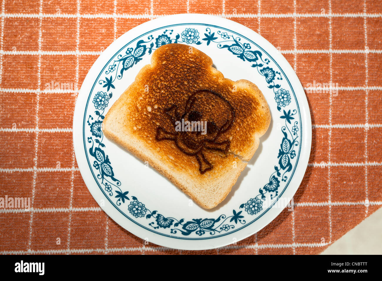 skull and crossed bones burned into a piece of toast on a plate. celiac disease Gluten Allergy Stock Photo