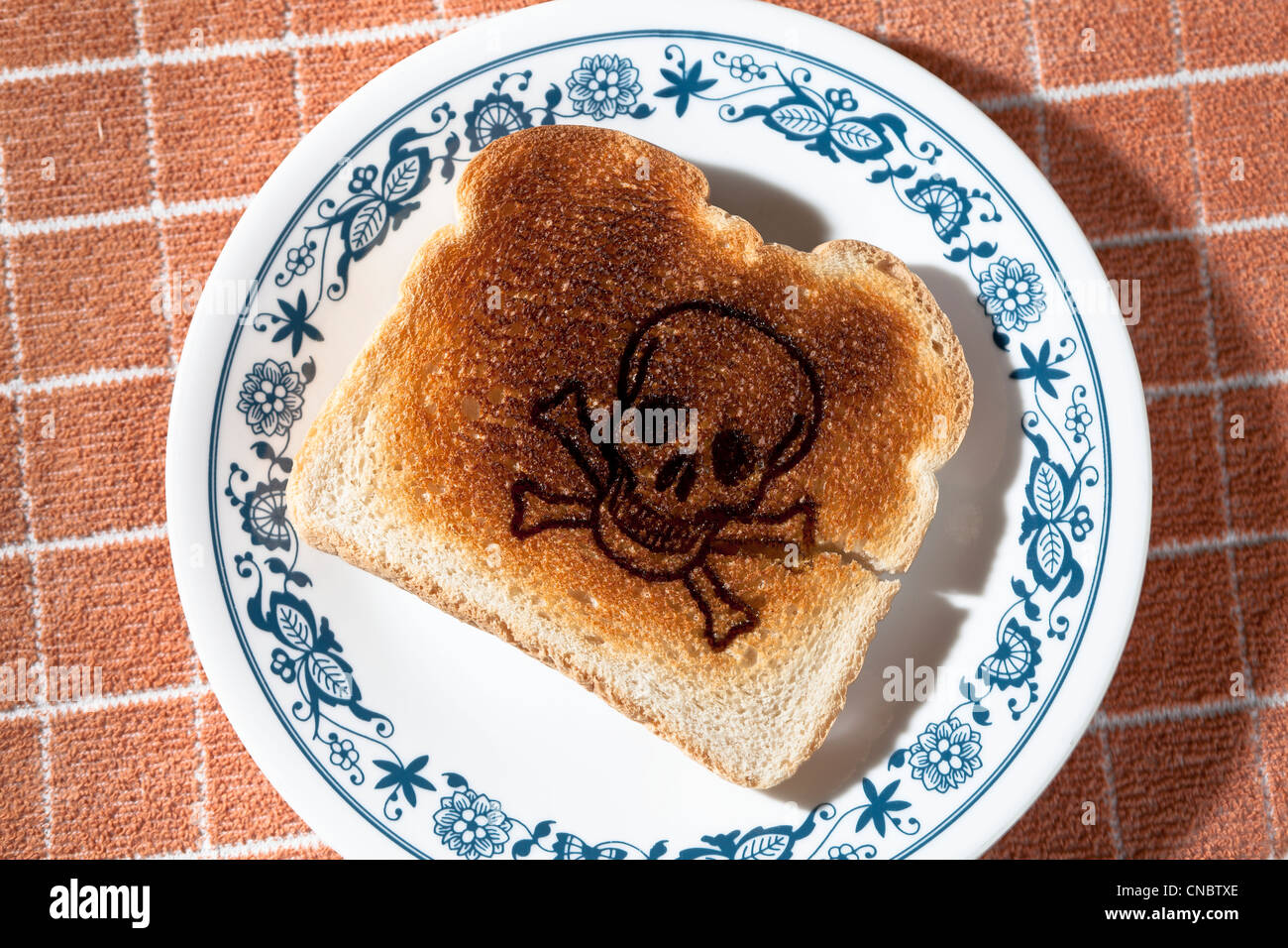 skull and crossed bones burned into a piece of toast on a plate. celiac disease Gluten Allergy Stock Photo