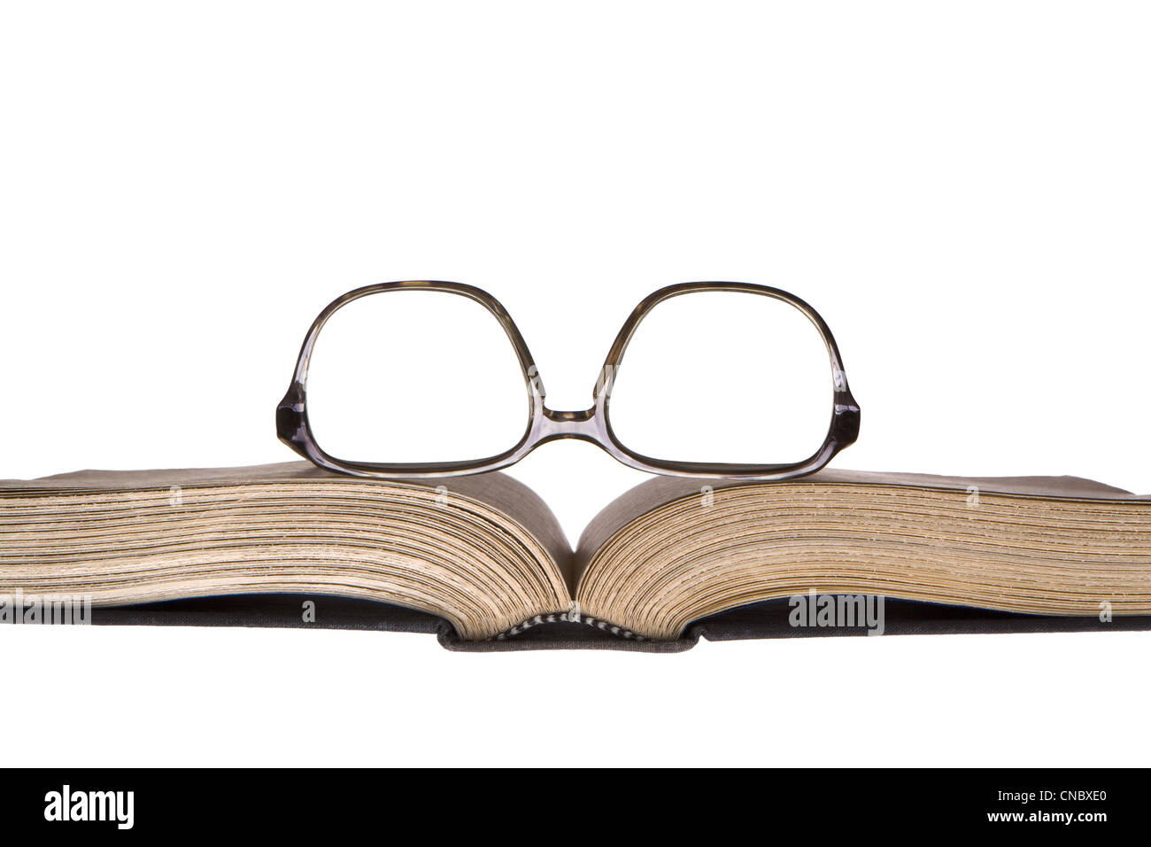 Old, upside-down eye glasses in plastic frame resting on old, yellowed open book. Frontal horizontal view. Isolated on white. Stock Photo