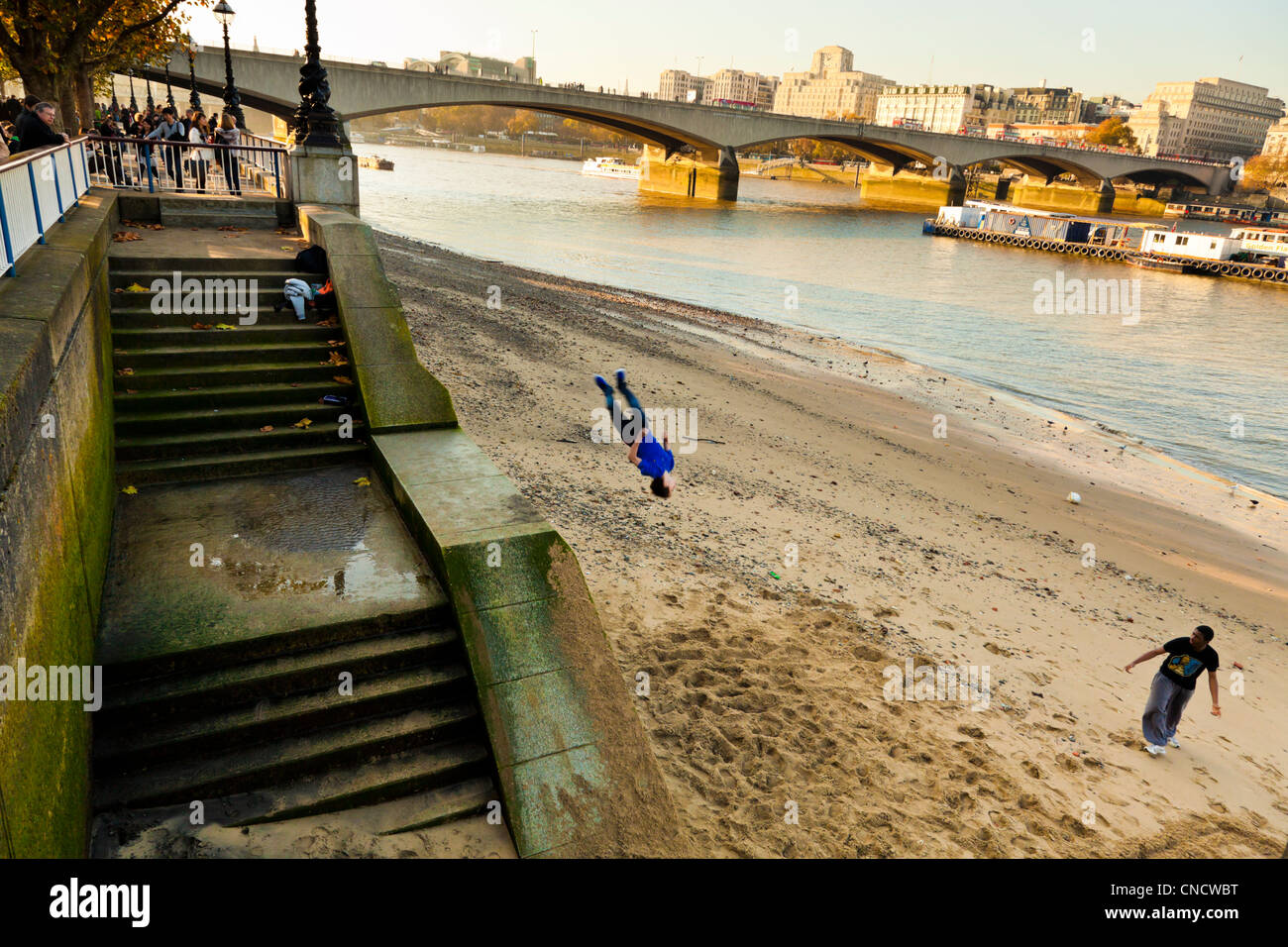 Boys playing, jumping and somersaulting onto the sand by the River Thames, London, England, UK Stock Photo