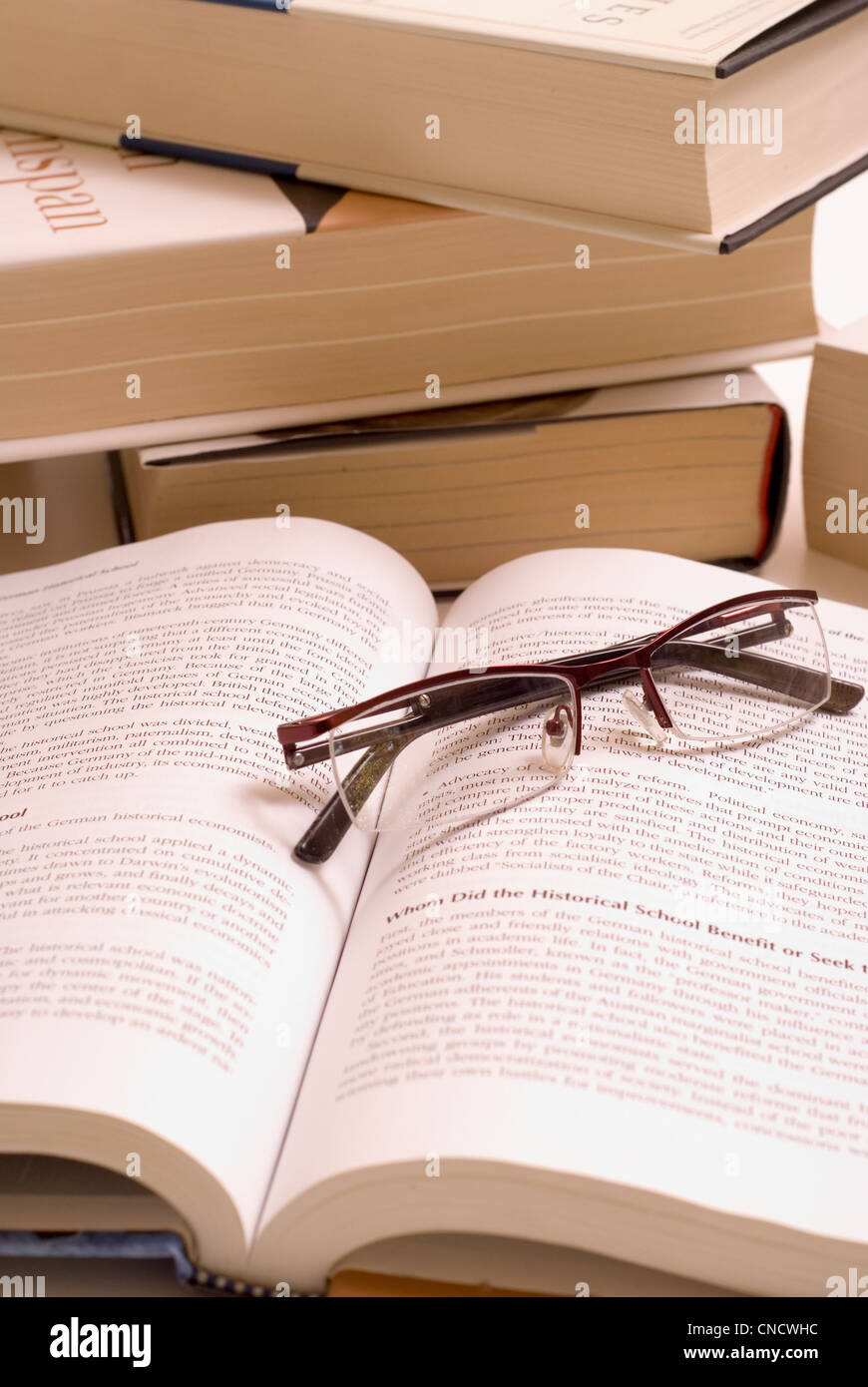 Pile of books with open book and reading glasses. Stock Photo