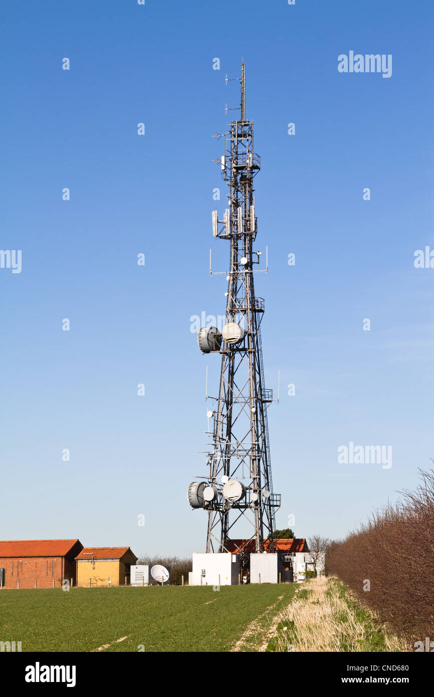 Telecomms tower with small buildings at it's base standing at the edge of a field. Stock Photo