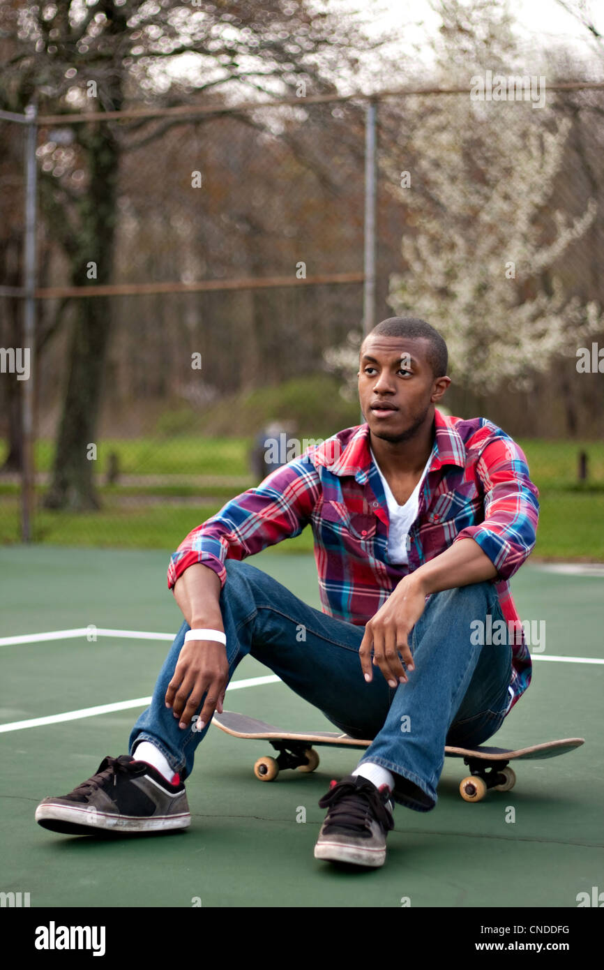 A young man hanging out in the tennis courts sitting on his skateboard