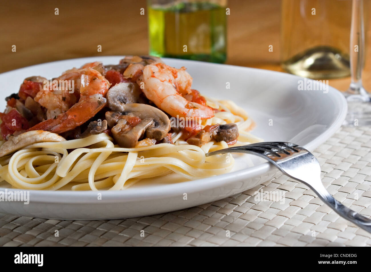 A delicious shrimp scampi pasta dish with mushrooms and diced tomatoes on a white plate. Shallow depth of field. Stock Photo