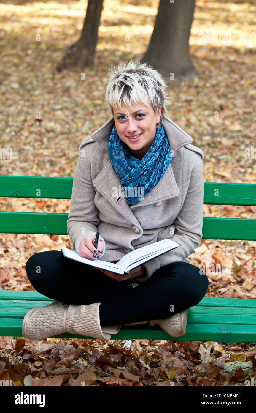 Portrait of young attractive smiling woman sitting on park bench and ...