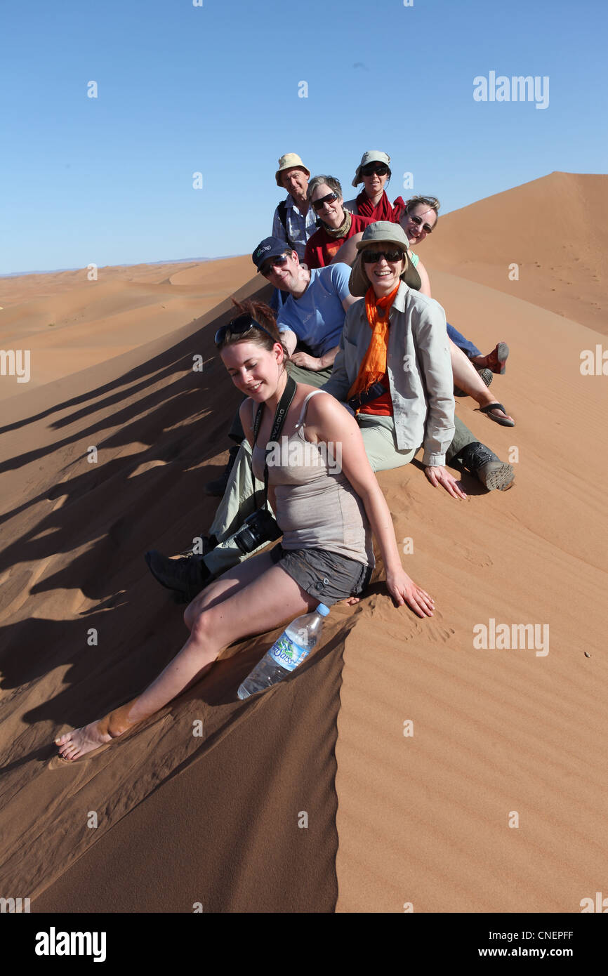 Tourists sitting atop a sand dune in the Sahara desert, southern ...