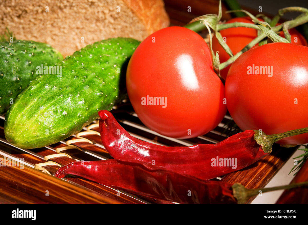 Three tomatoes, two cucmber and peppers with bread on wooden tray Stock Photo