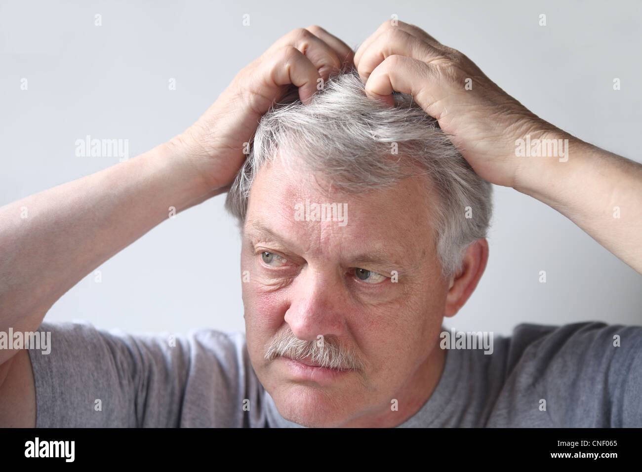 mature man uses both hands to scratch his head Stock Photo