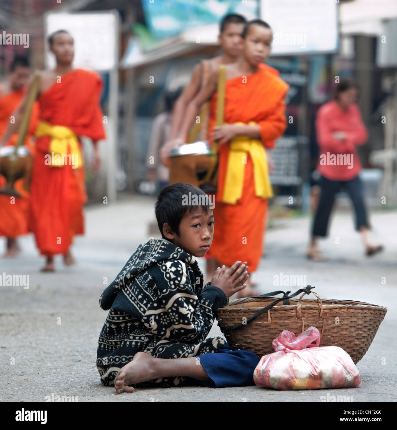 Young Lao boy begging for alms from passing Buddhist monks who have just received alms during morning alms procession Stock Photo
