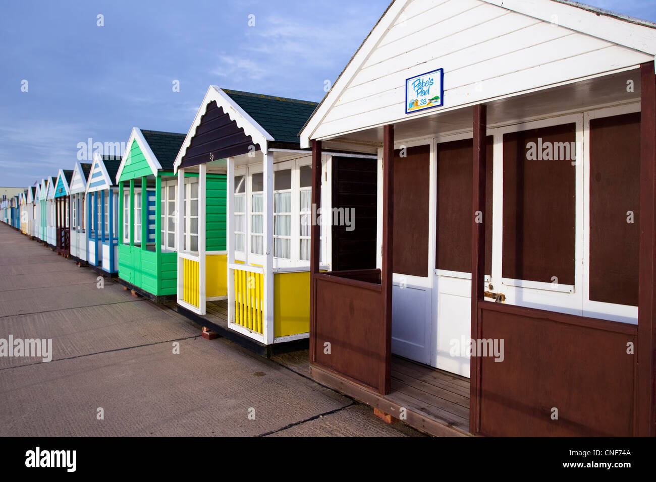 A row of different colored/coloured beach huts receding into the distance from the right to the left of the photo. Stock Photo