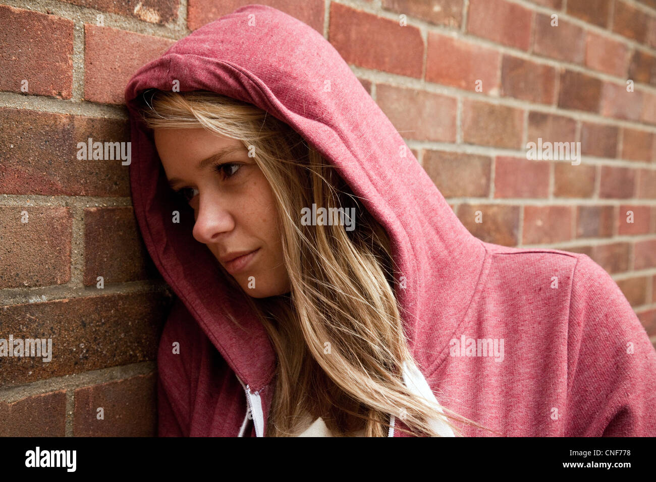 Blonde teenage girl wearing a hoodie leaning against a wall, Billericay Essex UK Stock Photo